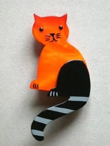 an orange cat sitting on top of a black and white striped brooch pin with eyes wide open