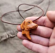 a person holding a small wooden dog on a leather cord necklace in their left hand