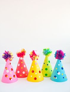 colorful party hats with pom poms on them are lined up against a white background