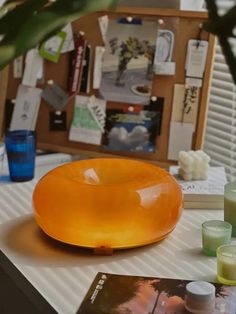 an orange glass bowl sitting on top of a table next to some candles and books