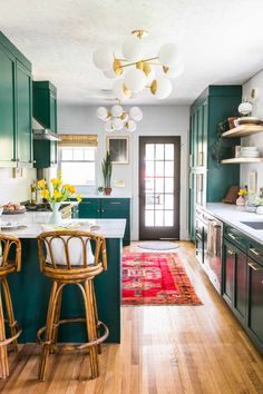 a kitchen with green cabinets and white counter tops, two stools in front of the island