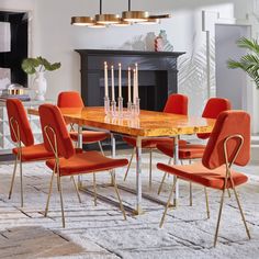 a dining room table with orange chairs and candles on the end tables in front of a fireplace