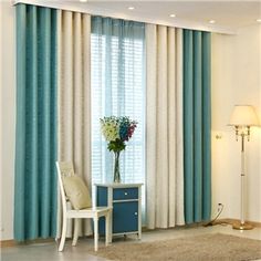 a living room with blue curtains and a white chair in front of a table with flowers on it