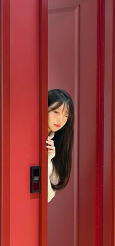 a woman is peeking out from behind a red door