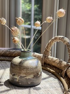 a vase with dried flowers in it sitting on a table next to a basket and window