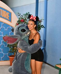 a woman in a black bathing suit hugging a gray stuffed animal with a red bow on her head