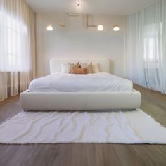 a large white bed sitting on top of a wooden floor next to two lamps above it