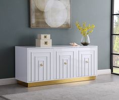 a white sideboard with gold trim and drawers in a living room next to a painting on the wall