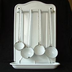 three white utensils hanging from the side of a rack on a black background