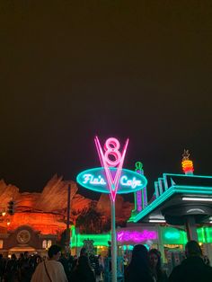 many people are walking around in front of the neon lights at an outdoor shopping mall