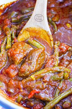 a wooden spoon in a stew with meat and green beans on the side, ready to be eaten