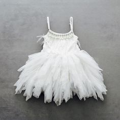 a white dress with feathers on the bottom is laying on a gray floor and there is no image to describe