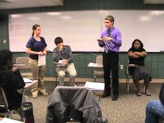 a group of people standing around each other in front of a class room full of people