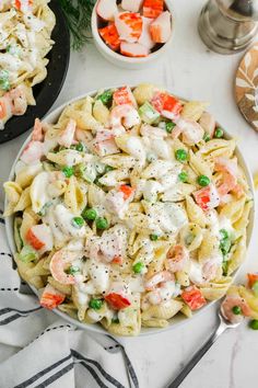 pasta salad with shrimp, peas and carrots in a white bowl on a table