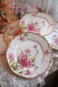 three plates with pink flowers on them sitting on a lace tablecloth next to a vase