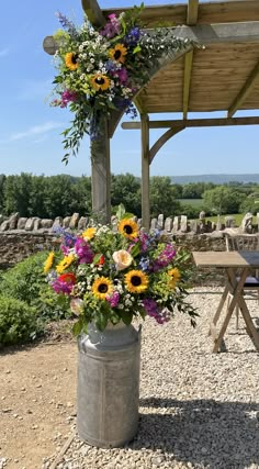 a large bucket filled with lots of flowers on top of a gravel covered ground next to a picnic table