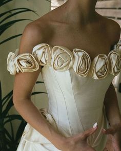 a woman in a white dress with flowers on her shoulder and hands behind her back