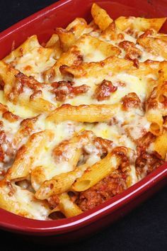 a red casserole dish filled with cheesy pasta and meat covered in sauce