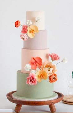 a multi - tiered cake with flowers on the top and bottom is sitting on a wooden stand