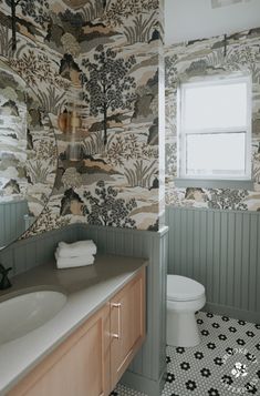 a bathroom with a toilet, sink and wall papered in animal designs on the walls