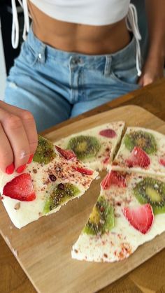 a person cutting up a piece of fruit pizza on top of a wooden cutting board