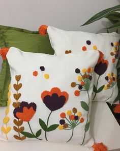 two white pillows with orange and green flowers on them sitting next to a potted plant