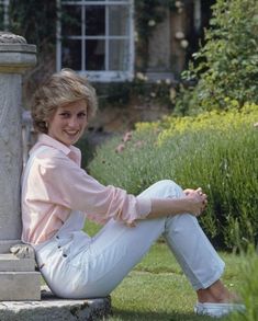 a woman sitting on the ground next to a stone pillar in front of a house