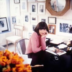 a woman sitting at a table in front of a mirror with pictures on the wall behind her