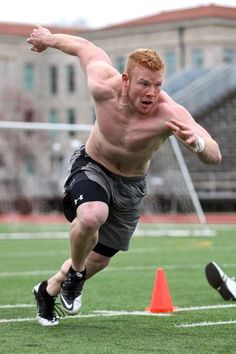 a shirtless man running across a field with an orange cone