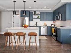 a kitchen with blue cabinets and stools in front of an island countertop that has three wooden barstools on it