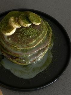 a stack of pancakes covered in green and white icing with bananas on the top