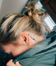 a woman with a tattoo on her left side behind her ear is looking down at the floor