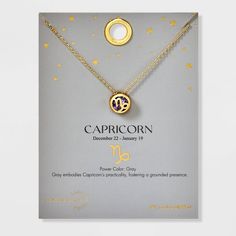 the capricorn necklace is displayed in front of a card with gold stars on it