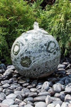 a rock sitting on top of a pile of rocks next to some bushes and trees