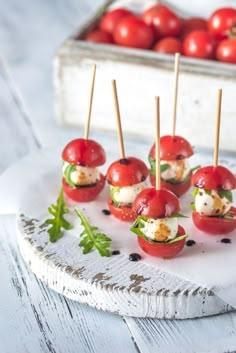 small appetizers with toothpicks and tomatoes on a white plate next to a tray of tomatoes