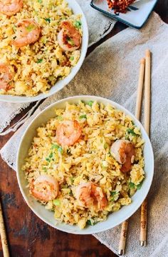 two bowls filled with shrimp and rice on top of a table next to chopsticks