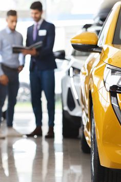 two men standing next to each other in a car showroom looking at their cars