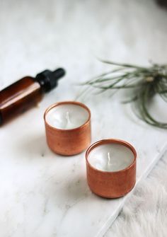 two candles sitting next to each other on a white surface with an essential oil bottle