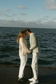 a man and woman standing next to each other near the ocean