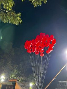 a bunch of red balloons floating in the air at night with lights shining on them