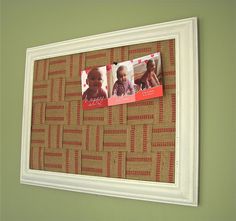 a white frame hanging on the wall above a baby's head with pictures pinned to it