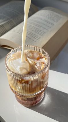 a drink being poured into a glass on top of a table next to an open book