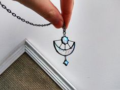 a person holding onto a chain with a pendant attached to it's end, in front of a white wall