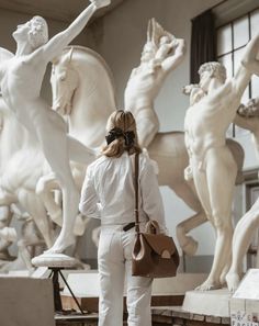 a woman standing in front of some white statues and holding a brown purse with her right hand