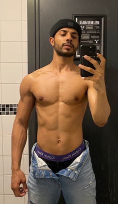 a shirtless man taking a selfie in front of a mirror with his cell phone