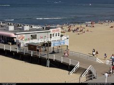 people are walking on the beach and in the water near a pier with a small restaurant