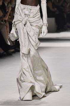 a woman in white is walking down the runway with her handbag on her hip