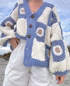 a woman standing on the beach wearing a blue and white crocheted cardigan