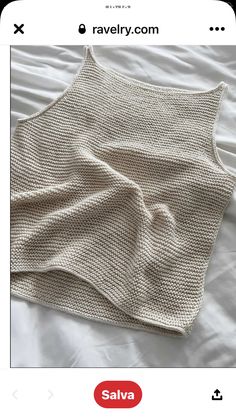 a knitted sweater laying on top of a white bed sheet with an unmade blanket