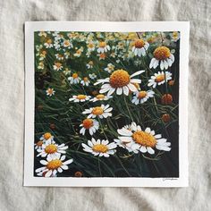 a painting of white and yellow daisies on a linen covered bed with grey sheets